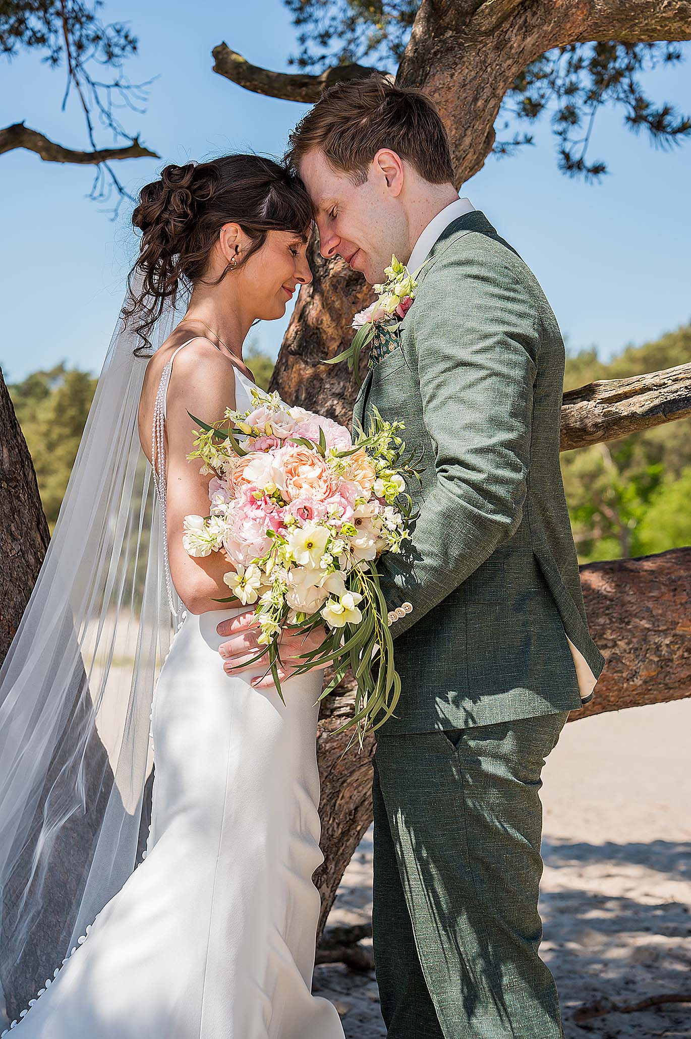 Bruidsfotograaf fotografeert bruidspaar met kleurrijk boeket bij een mooie boom