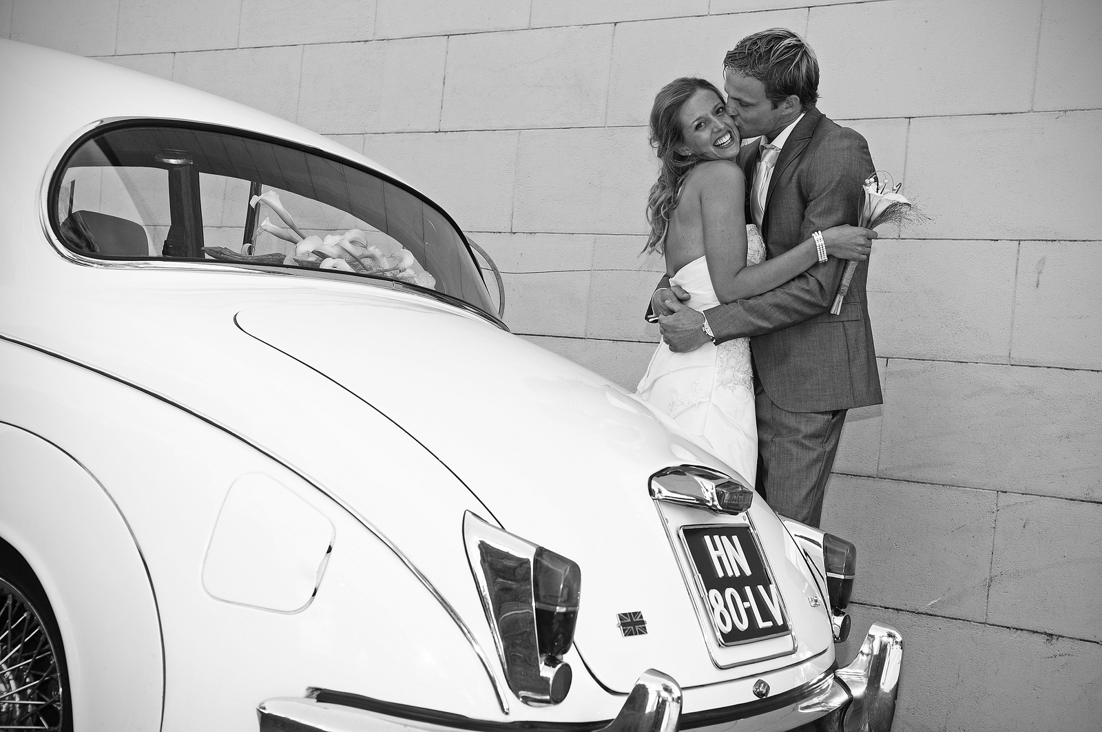 Zwart wit foto met daarop een bruidspaar naast een oude witte Jaguar MK2 2.4 trouwauto uit 1961