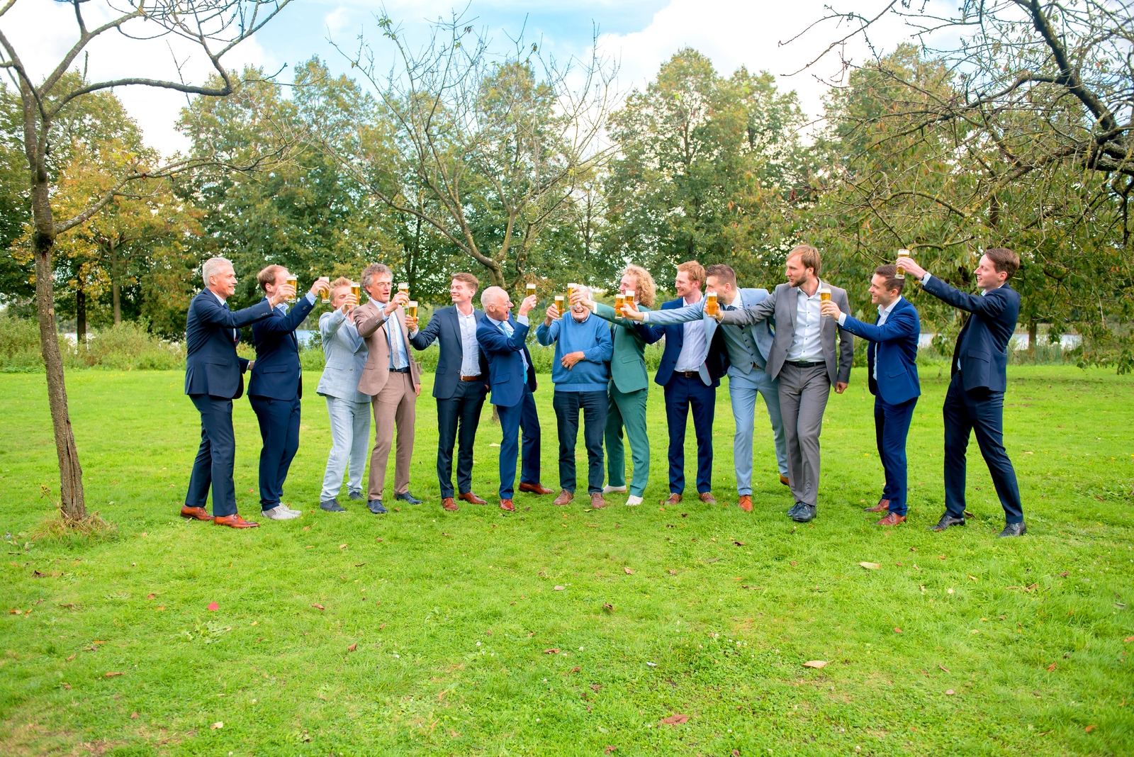 Mannen op bruiloft staan buiten in het gras te proosten met glazen bier