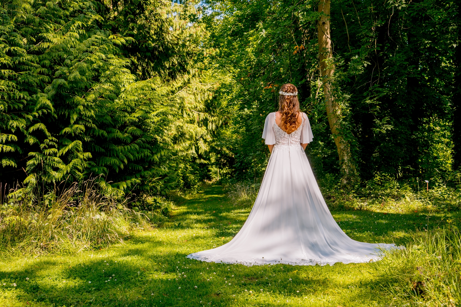 Bruid in witte trouwjurk met lange sluier staat te poseren in het mooie bos
