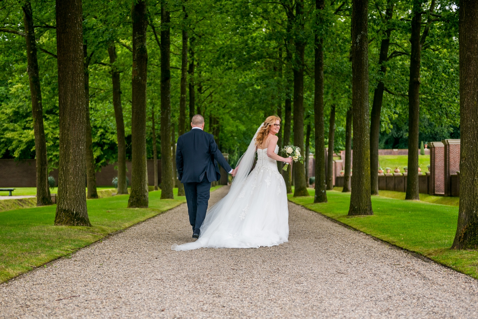 Bruid en bruidegom lopen hand in hand in de grote koninklijke tuin van Het Loo in Apeldoorn