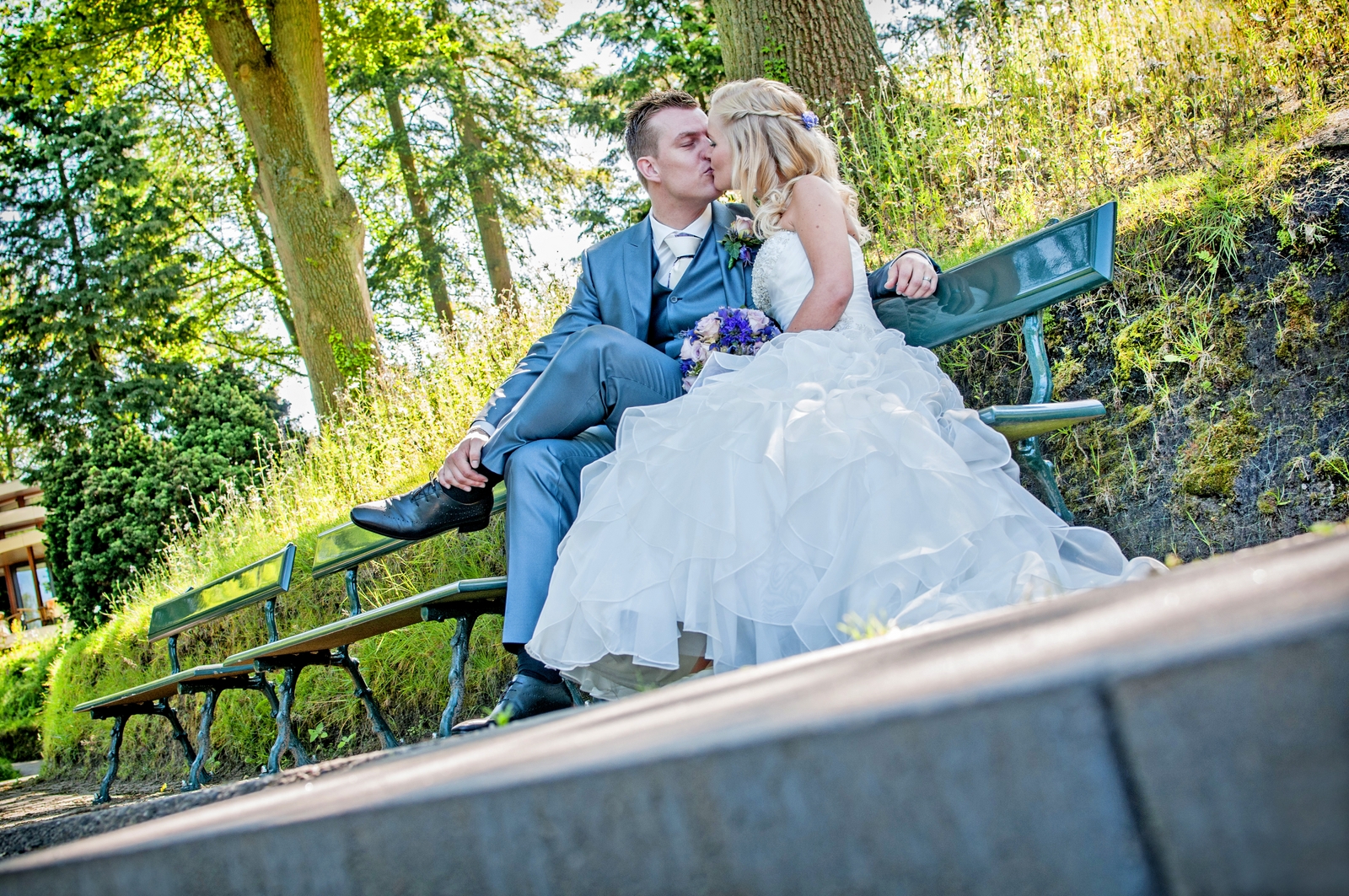 Vrolijk bruidspaar zit op een bankje in Lumido in Park Berg en Bos bij de Apenheul in Apeldoorn