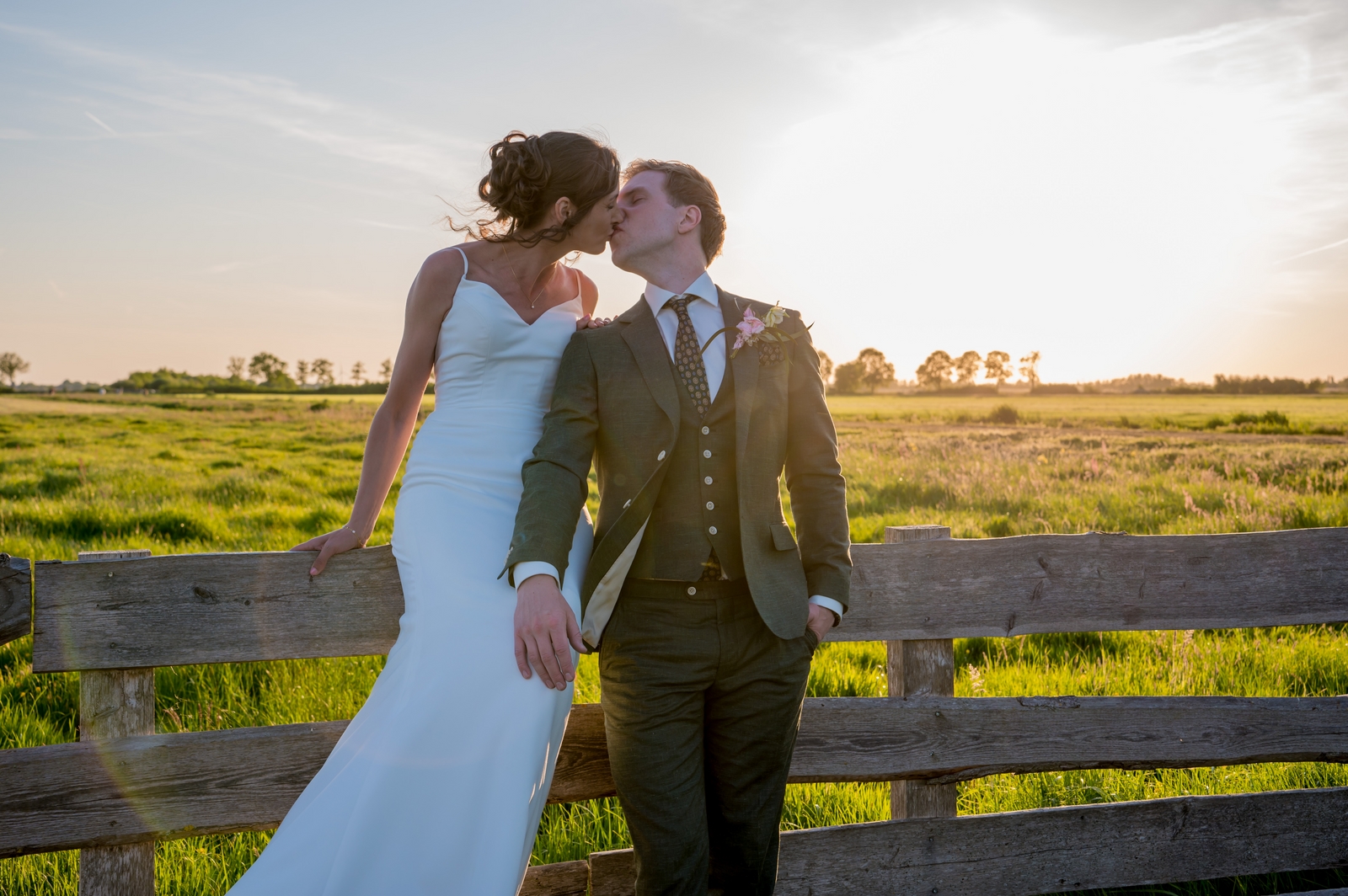 Bruidspaar zit op een hek bij zonsondergang in het prachtige boeren landschap bij Hoeve Landzicht in Nieuwer Ter Aa